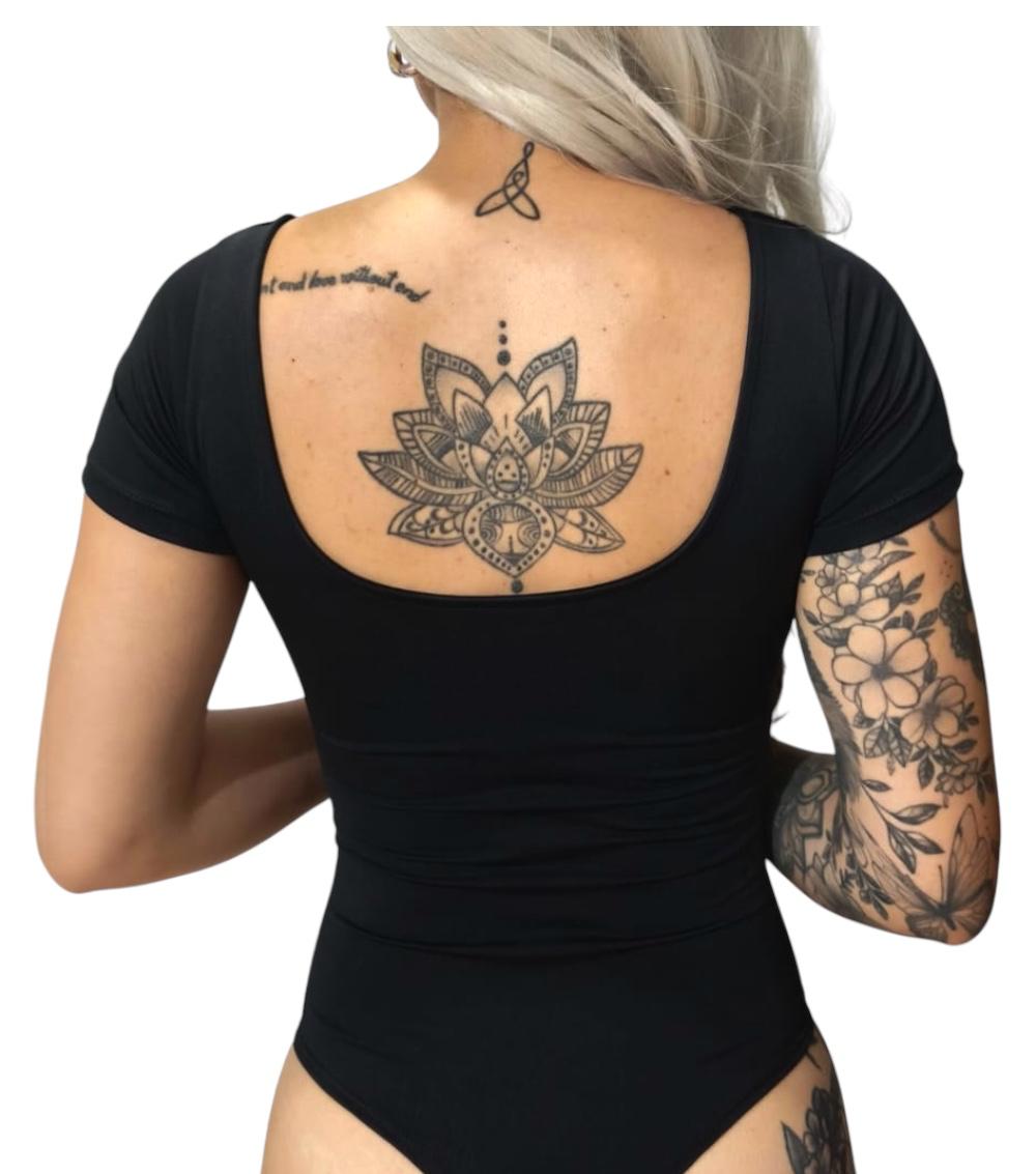 Body manga corta negro con tatuajes de flor de loto y flores en la espalda y brazo.