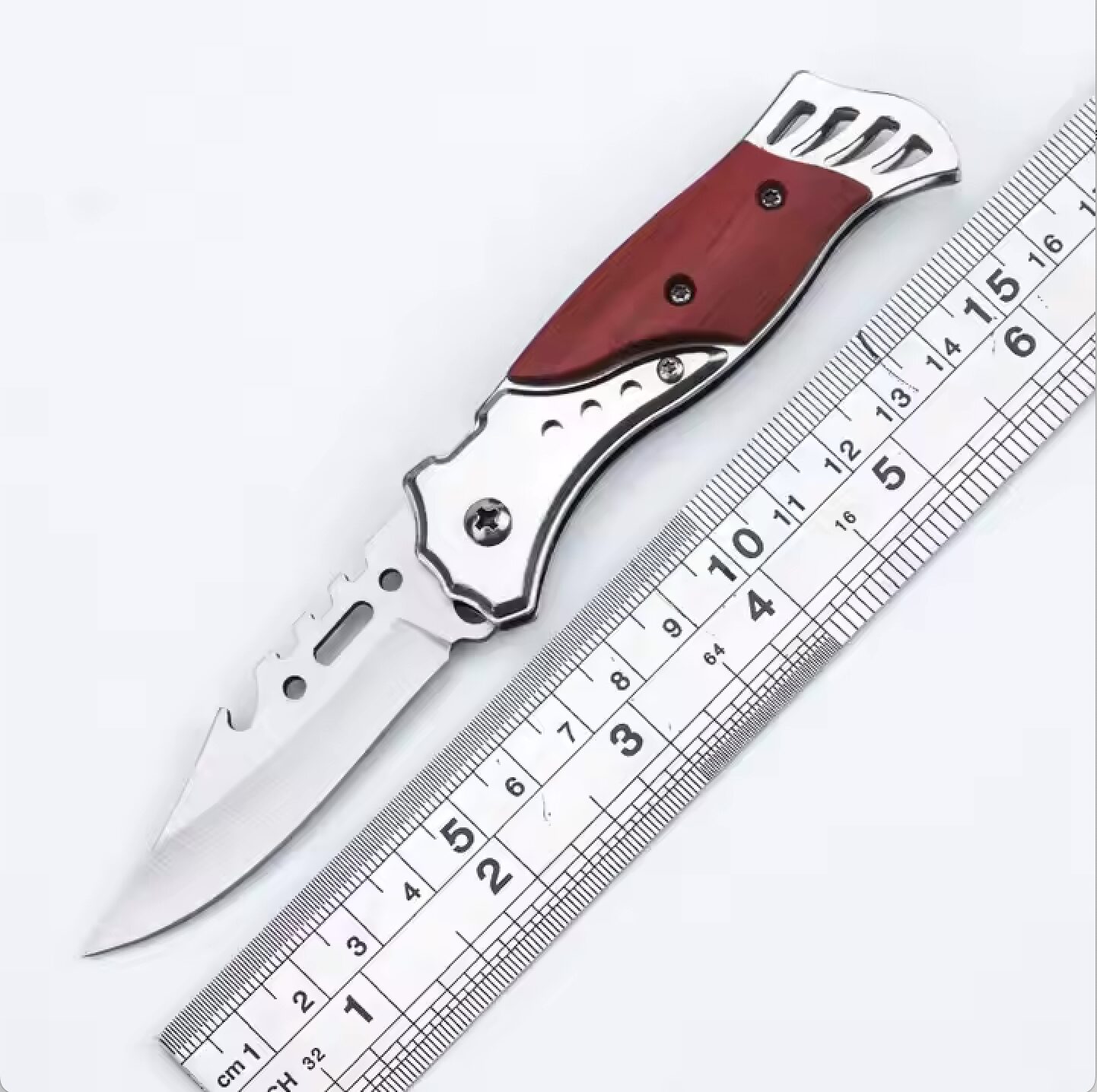 Navaja táctica plegable con mango de madera roja y detalles metálicos plateados, junto a una regla de 16 pulgadas.
