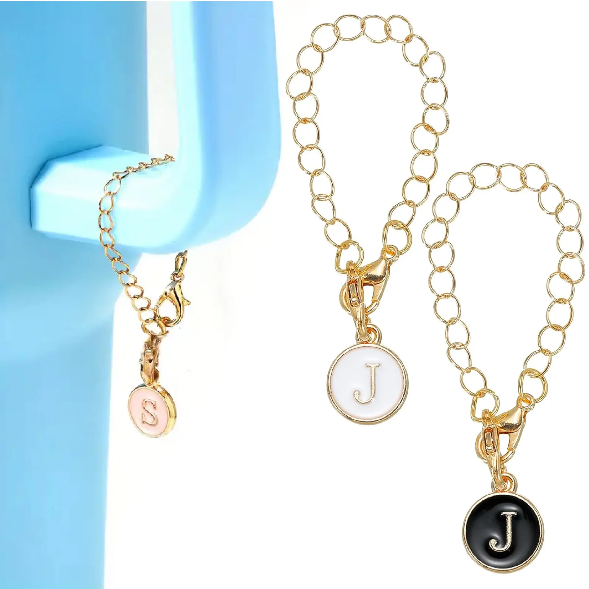 Dos pulseras doradas con dije de inicial, una 'S' rosa y dos 'J', una blanca y otra negra.
