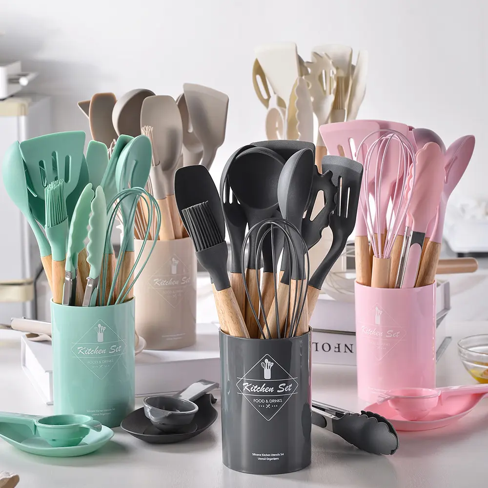 Set de 12 utensilios de cocina con mangos de madera y puntas de silicona en colores menta, gris y rosado, organizados en contenedores cilíndricos a juego.