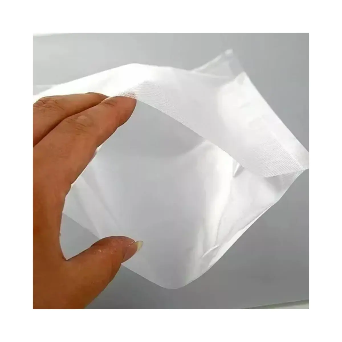 Mano abriendo bolsa empacadora al vacío blanca, material no tejido resistente, ideal para alimentos.