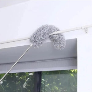 Plumero extensible de microfibra gris curvado limpiando el borde superior de una ventana con marco blanco.