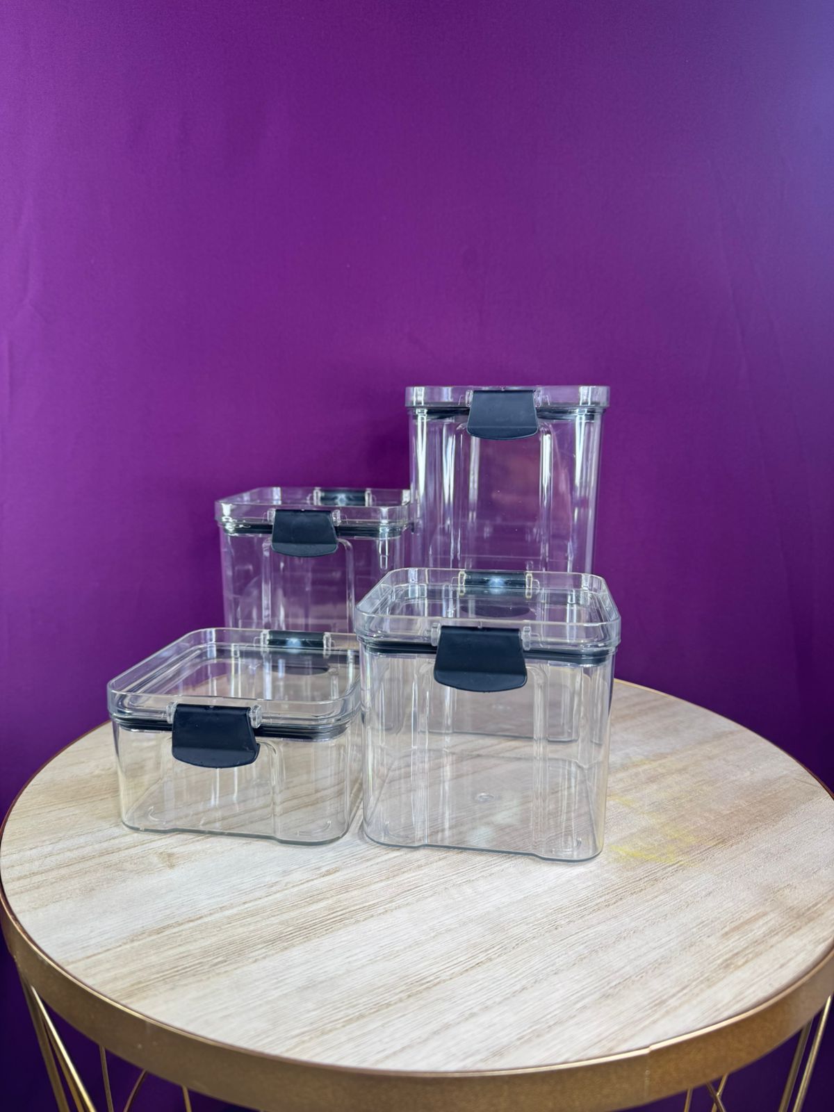 Juego de 4 organizadores de cocina transparentes con tapas negras, sobre mesa rústica y fondo morado.