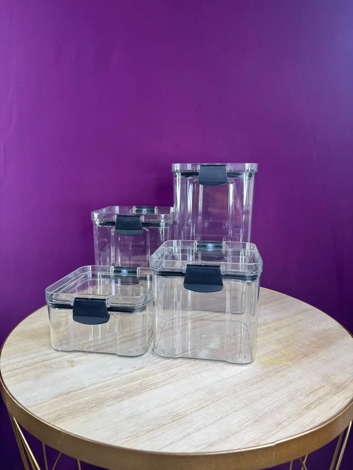 Juego de 4 organizadores de cocina transparentes con tapas negras, sobre mesa rústica y fondo morado.