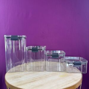 Organizador de cocina X4, recipientes rectangulares transparentes con tapas negras, apilables en mesa redonda.