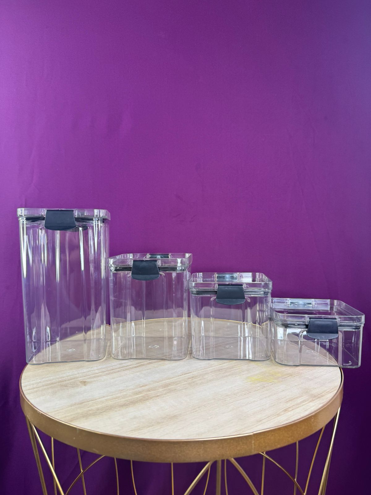 Organizador de cocina X4, recipientes rectangulares transparentes con tapas negras, apilables en mesa redonda.