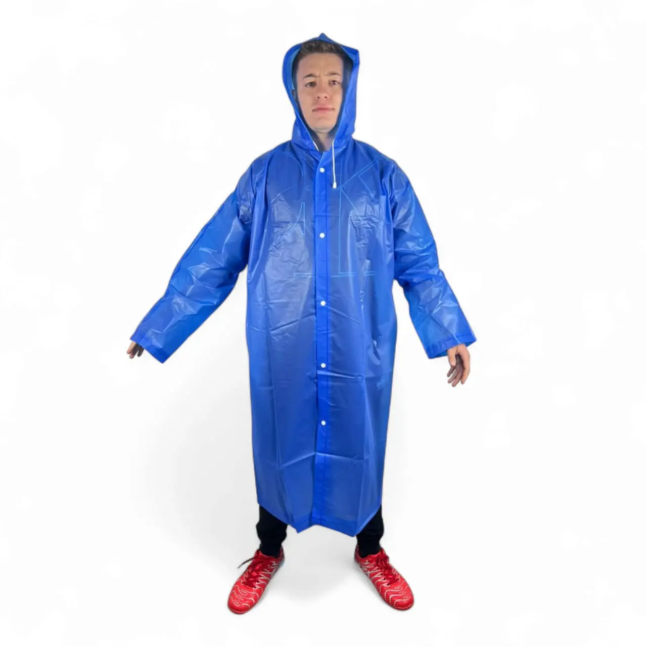 Hombre joven con capa impermeable azul brillante, con capucha, botones al frente y zapatillas rojas.
