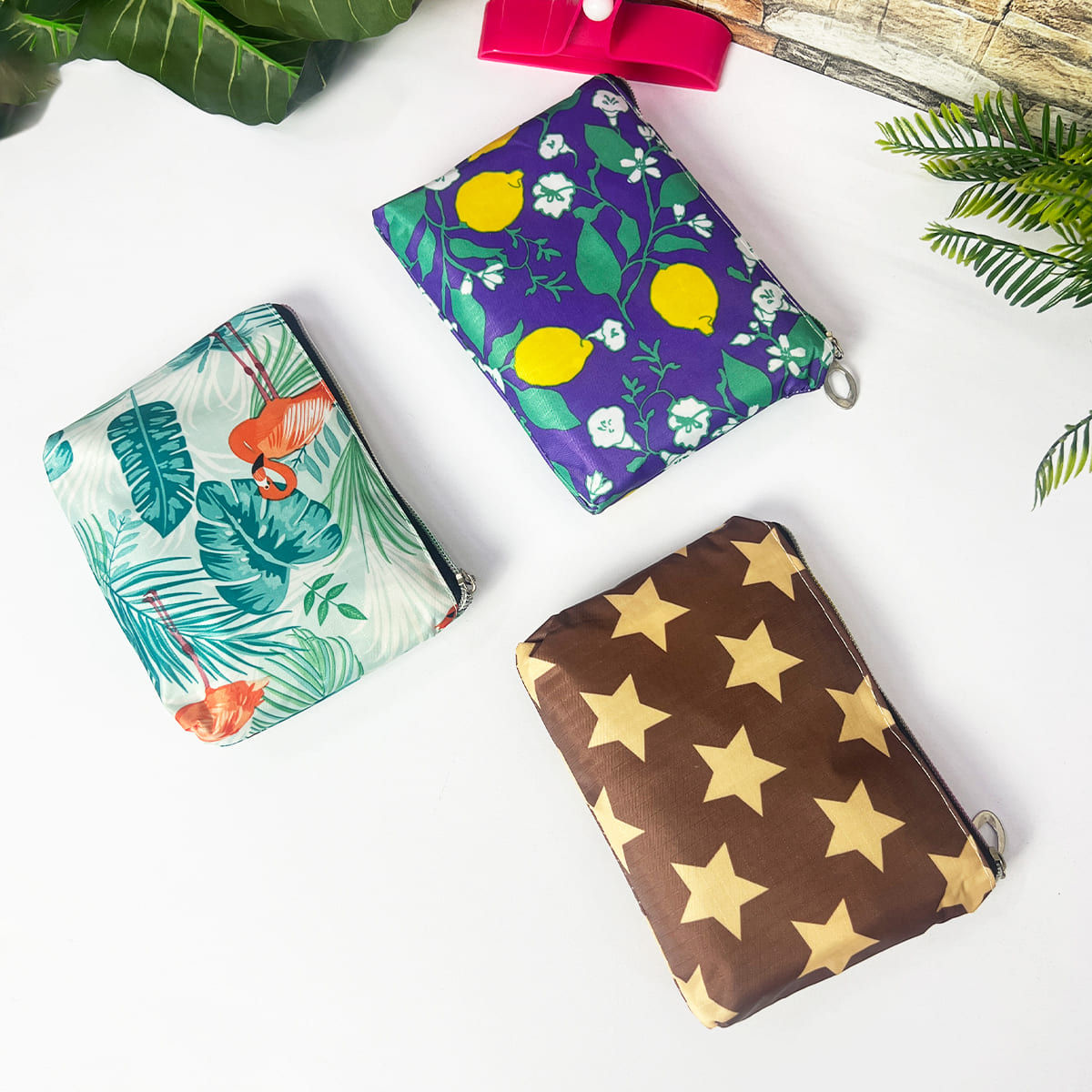 Set de 2 bolsas reutilizables plegables: una con flamencos y hojas tropicales, otra con limones morados y flores, y una más café con estrellas doradas.