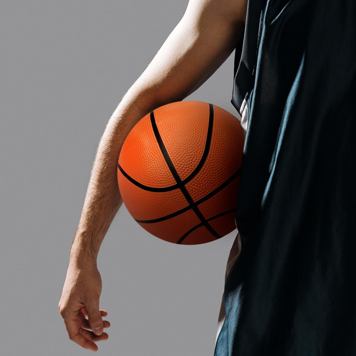 Balón de baloncesto naranja en mano de jugador con uniforme, textura visible, tamaño estándar.