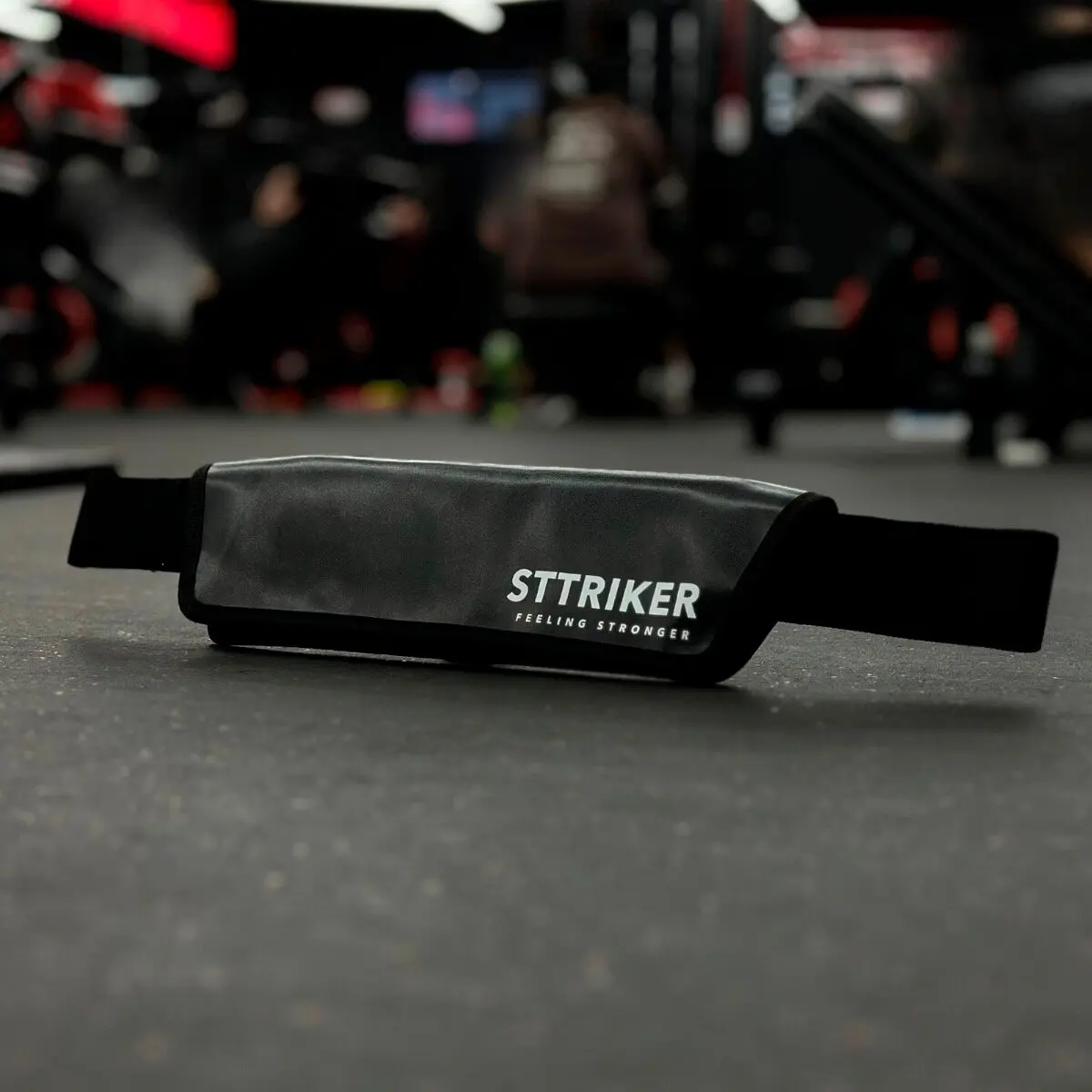 Cinturón STTRIKER para hip thrust, glúteos y pesas, en cuero sintético negro, sobre piso de gimnasio.