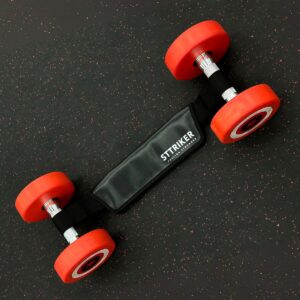 Pesas de mano con extremos rojos, conectadas por un cinturón negro de STTRIKER sobre superficie oscura con motas.