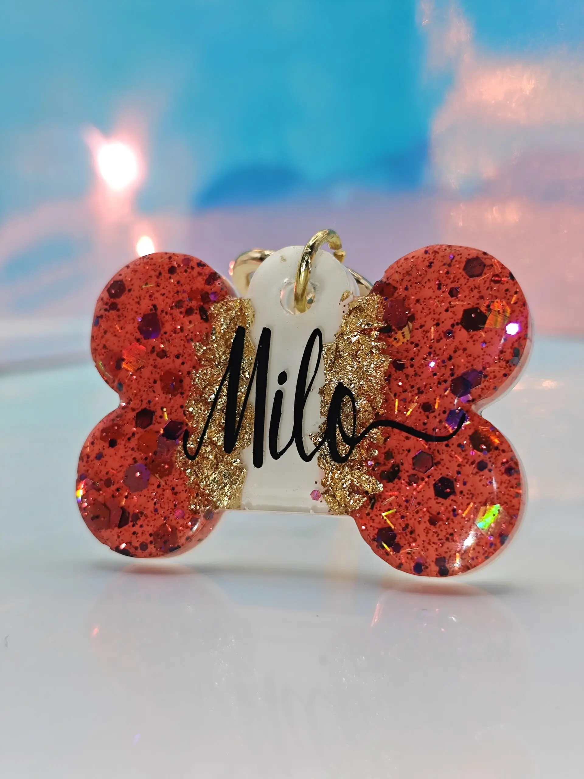 Placa de mascota hueso rojo con glitter dorado y nombre "Milo" grabado.