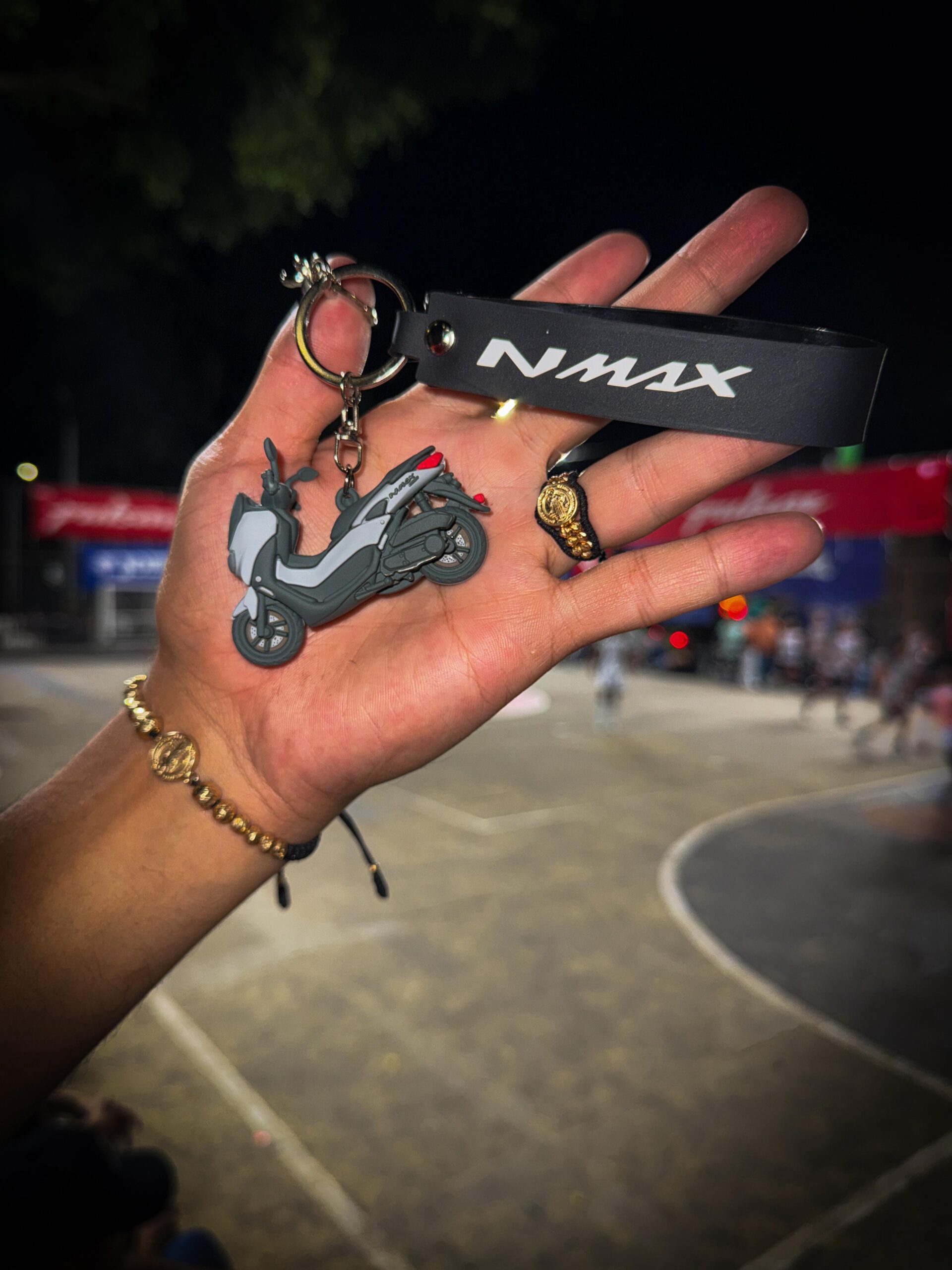 Llavero en 3D de moto NMAX gris y negro con detalle rojo, junto a un anillo y pulsera de oro en una mano.