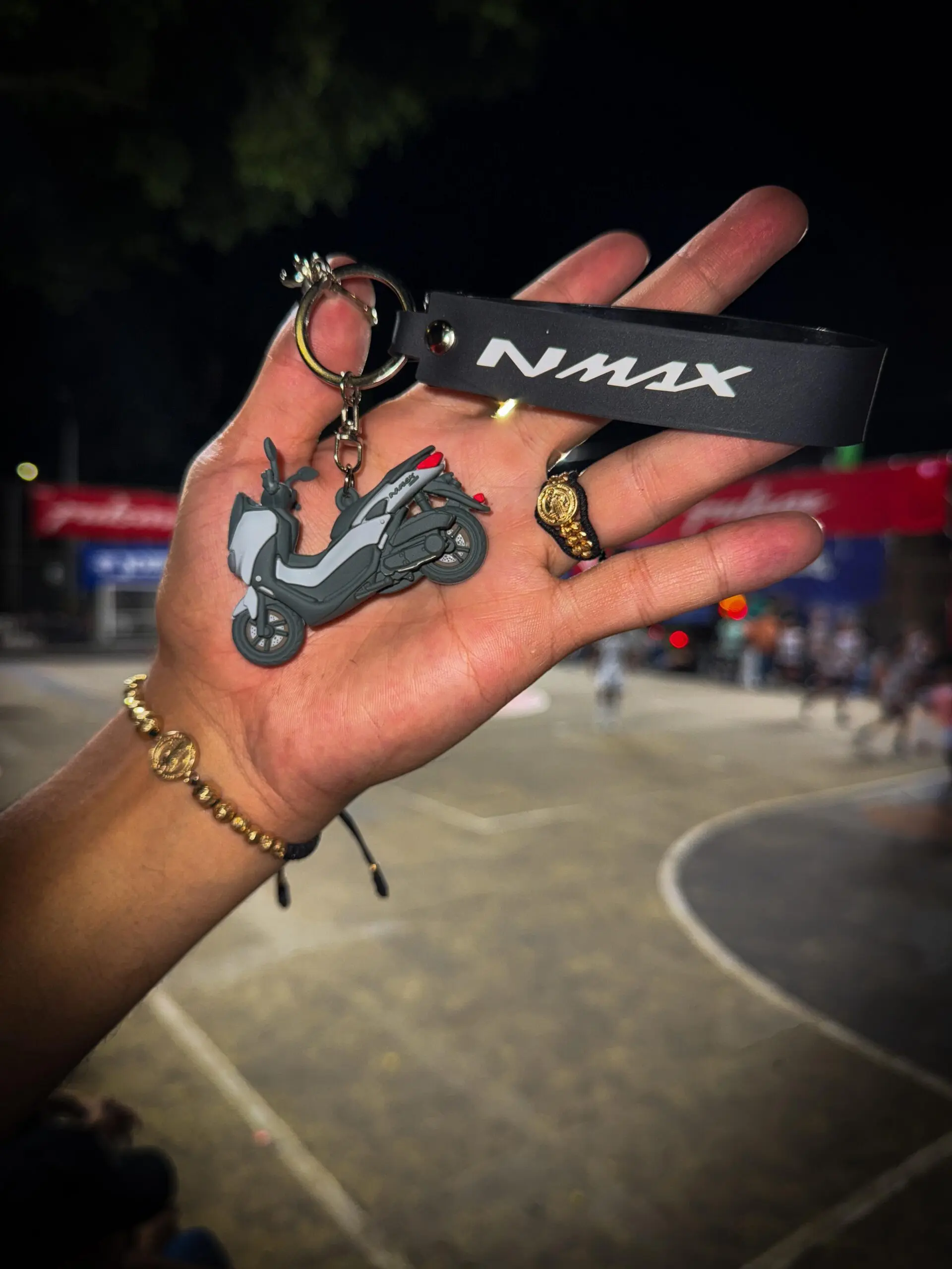 Llavero en 3D de moto NMAX gris y negro con detalle rojo, junto a un anillo y pulsera de oro en una mano.