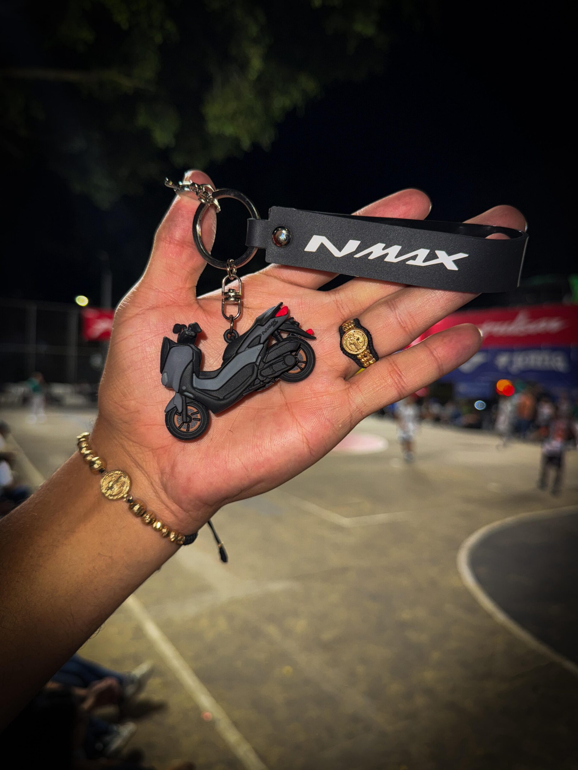 Llavero 3D negro de moto NMAX en mano con pulsera dorada.