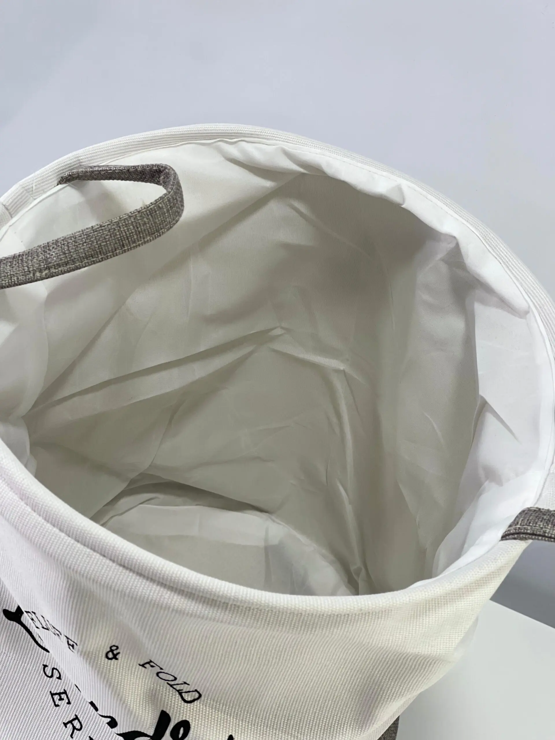 Cesto de ropa sucia de tela, blanco con detalles grises, interior blanco, vista desde arriba.