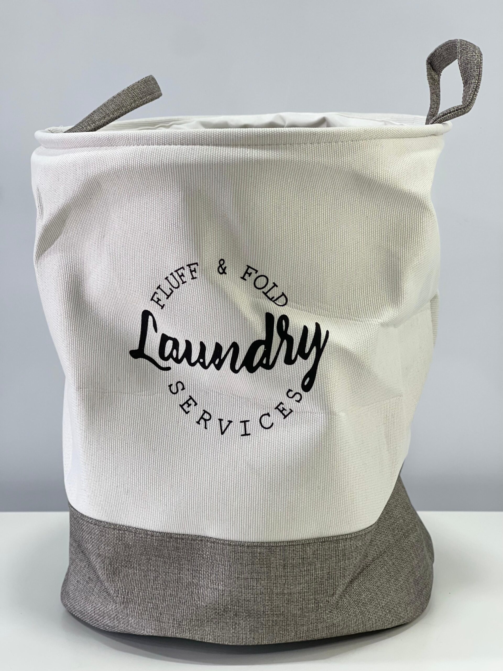 Cesto de tela para ropa sucia, blanco con base gris, diseño minimalista con texto "Laundry Services".