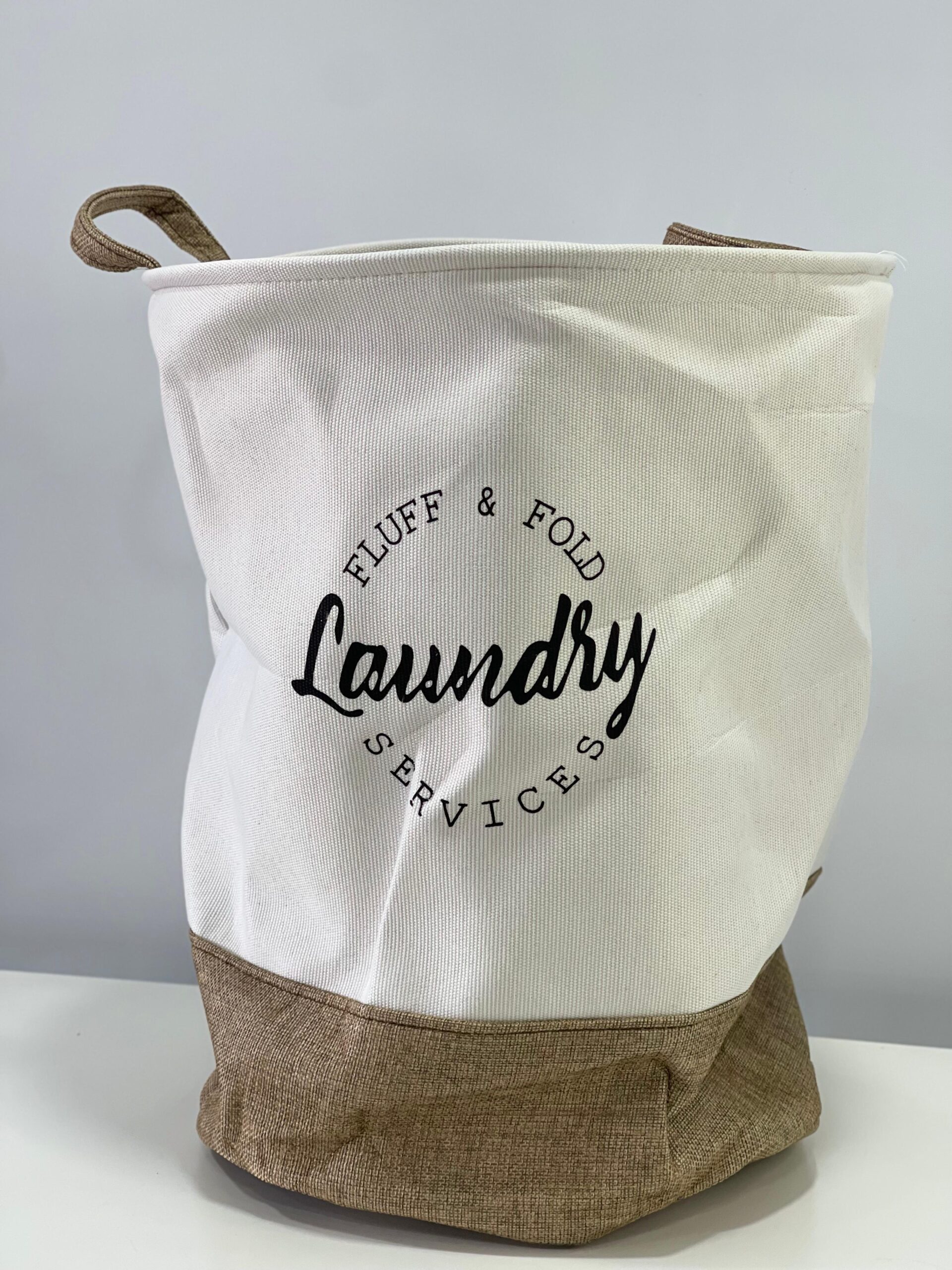 Cesto de tela gris y blanco para ropa sucia, con diseño minimalista y texto "Laundry Services".