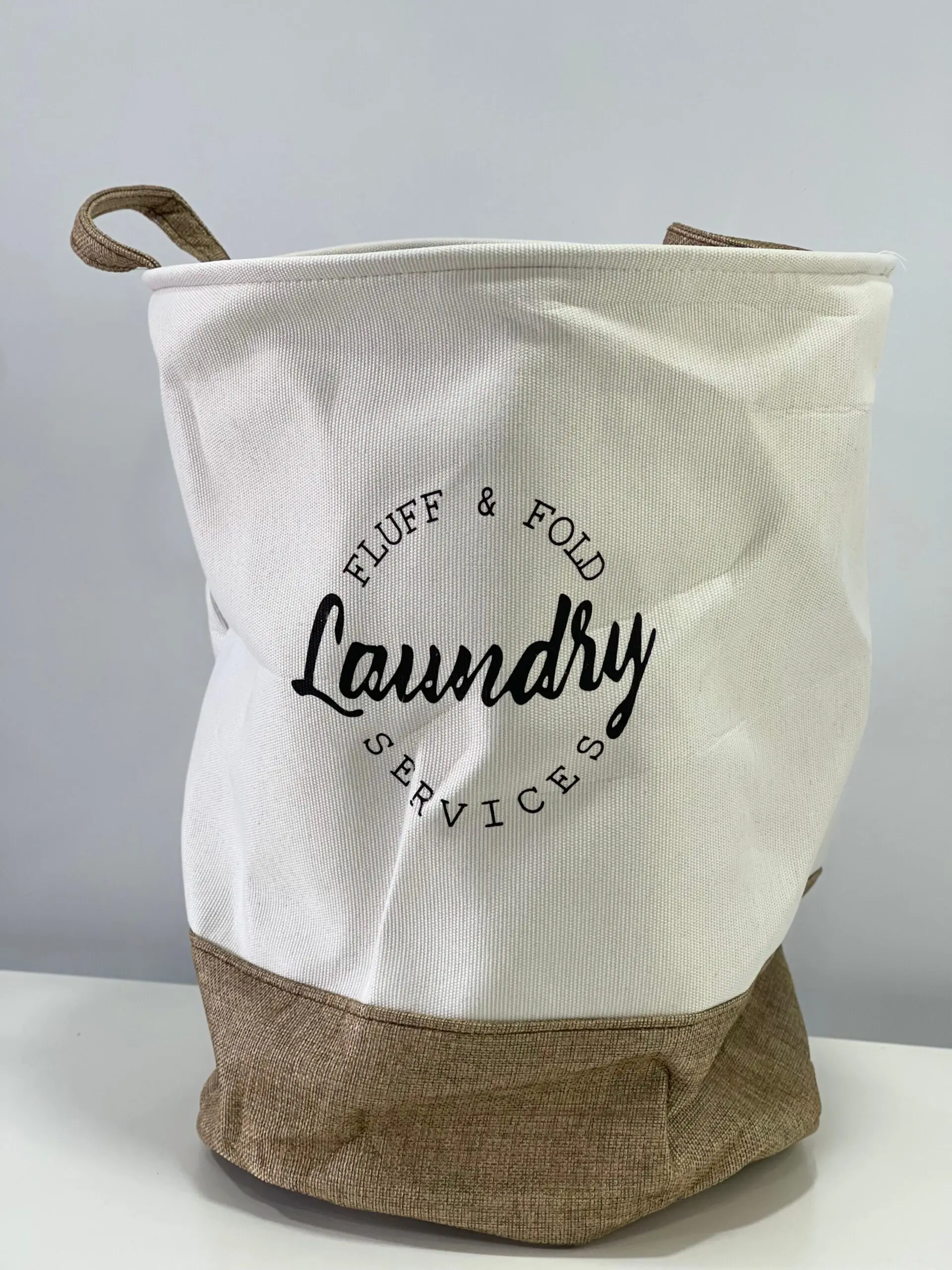 Cesto de tela gris y blanco para ropa sucia, con diseño minimalista y texto "Laundry Services".