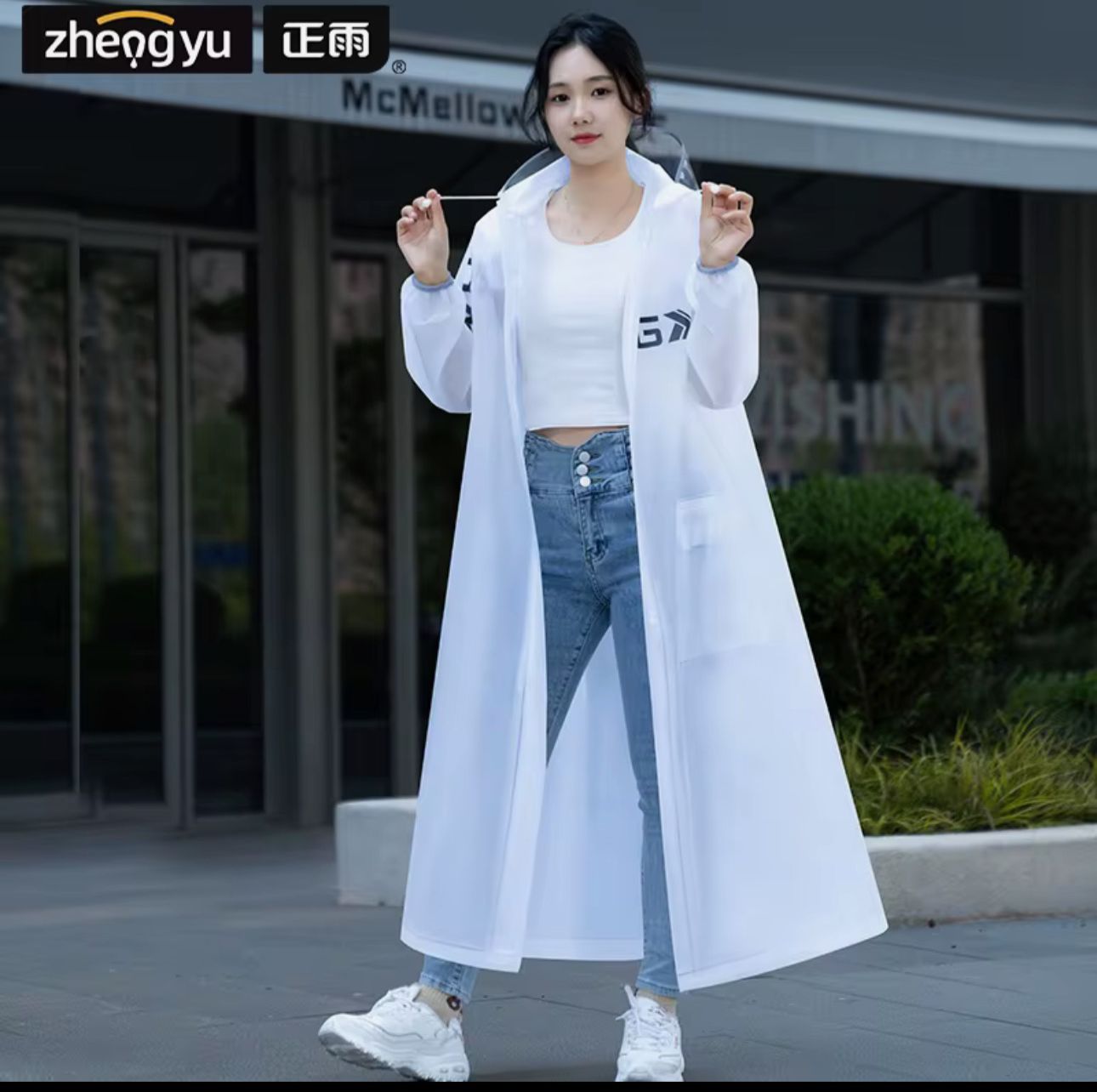 Mujer joven con impermeable blanco largo y transparente, capota y jeans, camina en exterior.
