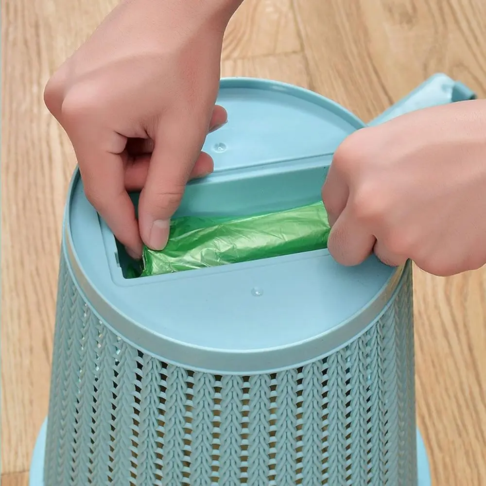 Manos colocando bolsa verde en papelera azul con diseño tejido y dispensador integrado.