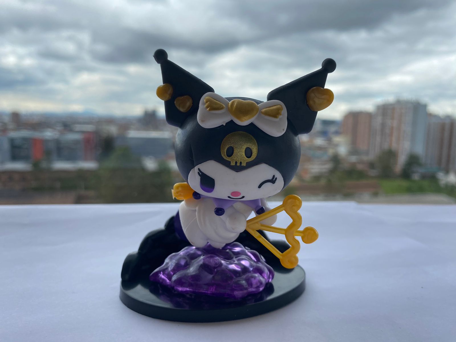 Figura miniatura Kuromi con arco y flecha dorados, posando sobre nube morada brillante.