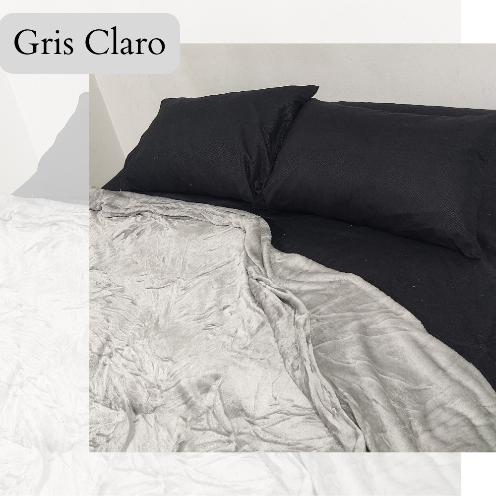 Cobija Piel de Durazno Gris Claro 1.40, doblada sobre cama negra con almohadas a juego.