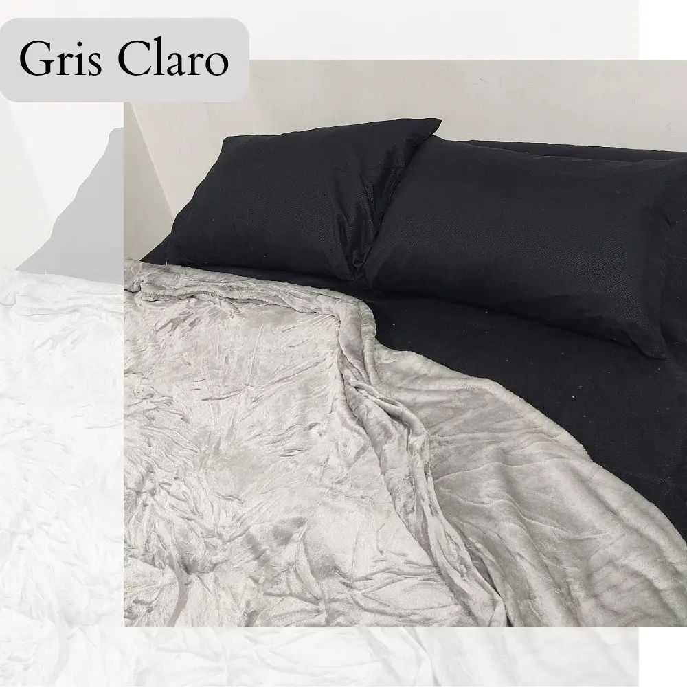 Cobija Piel de Durazno Gris Claro 1.40, doblada sobre cama negra con almohadas a juego.