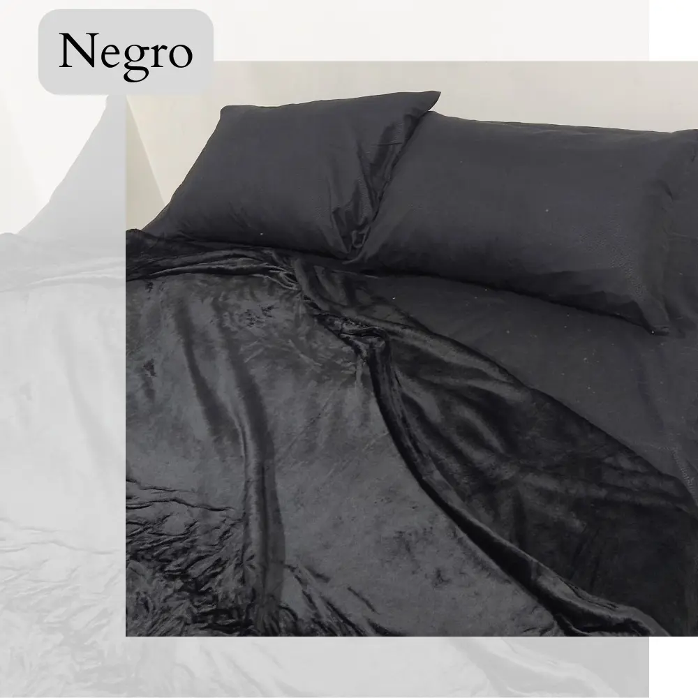Cobija piel de durazno negra, tamaño 1.40, textura suave y mullida, con dos almohadas negras encima.