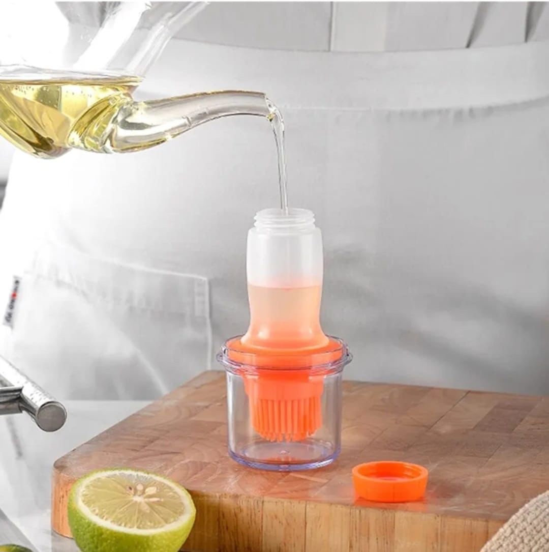 Dispensador de aceite transparente con brocha naranja, llenándose de aceite dorado.