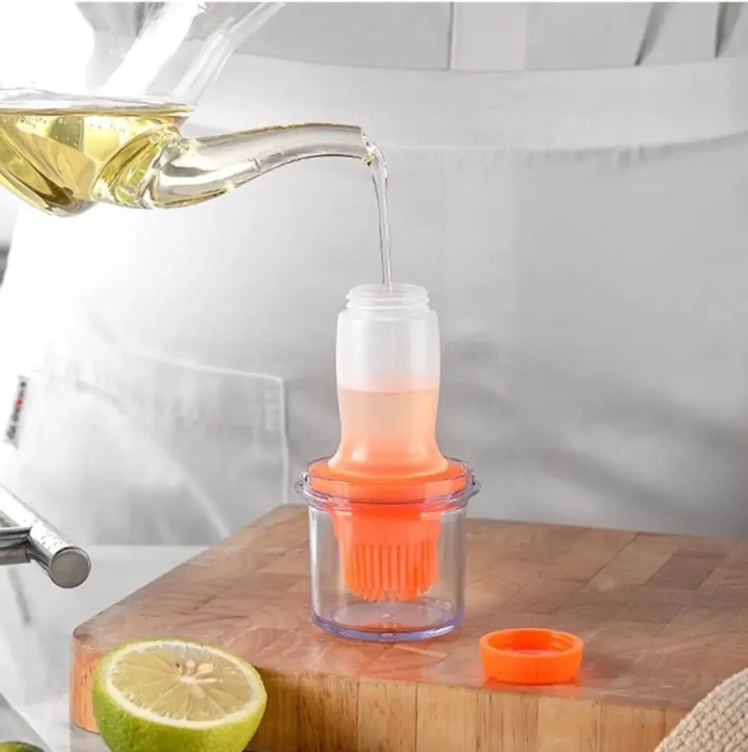 Dispensador de aceite transparente con brocha naranja, llenándose de aceite dorado.