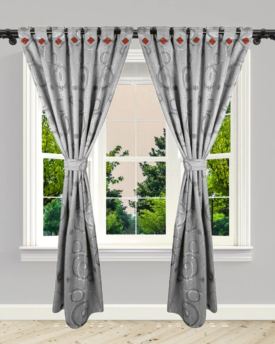 Cortinas grises con diseño jacquard y detalles rojos, atadas con pretina, sobre ventana con vista a árboles.