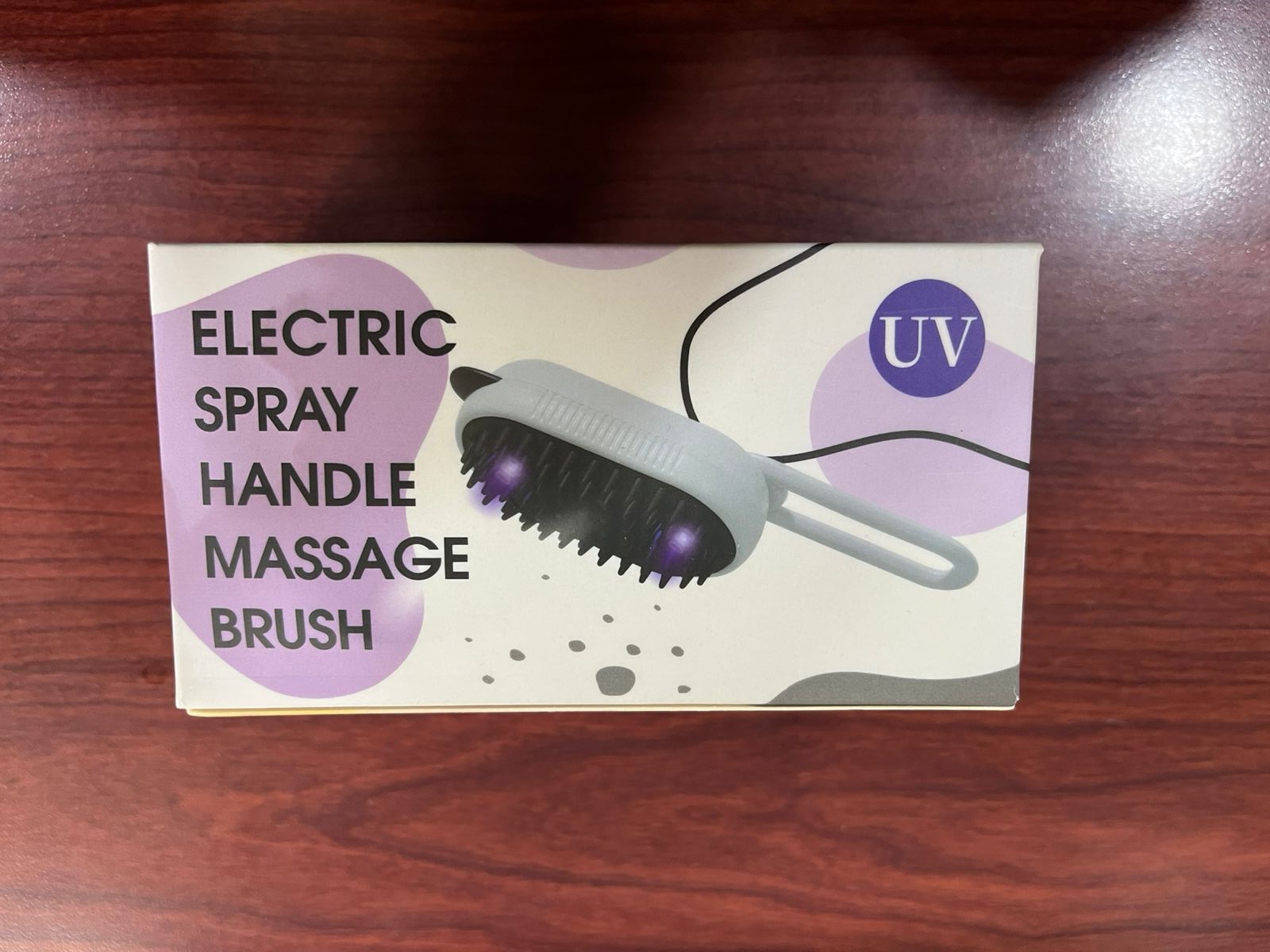Cepillo eléctrico gris con cerdas negras, luces moradas y letreros "UV" y "ELECTRIC SPRAY HANDLE MASSAGE BRUSH" en caja.