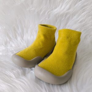 Zapatos respetuosos amarillos para bebé con suela de goma, sobre fondo blanco peludo.