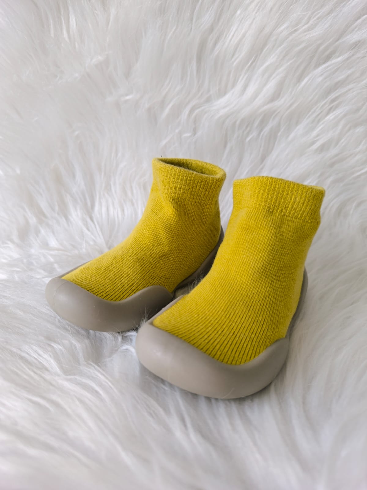 Zapatos respetuosos amarillos para bebé con suela de goma, sobre fondo blanco peludo.