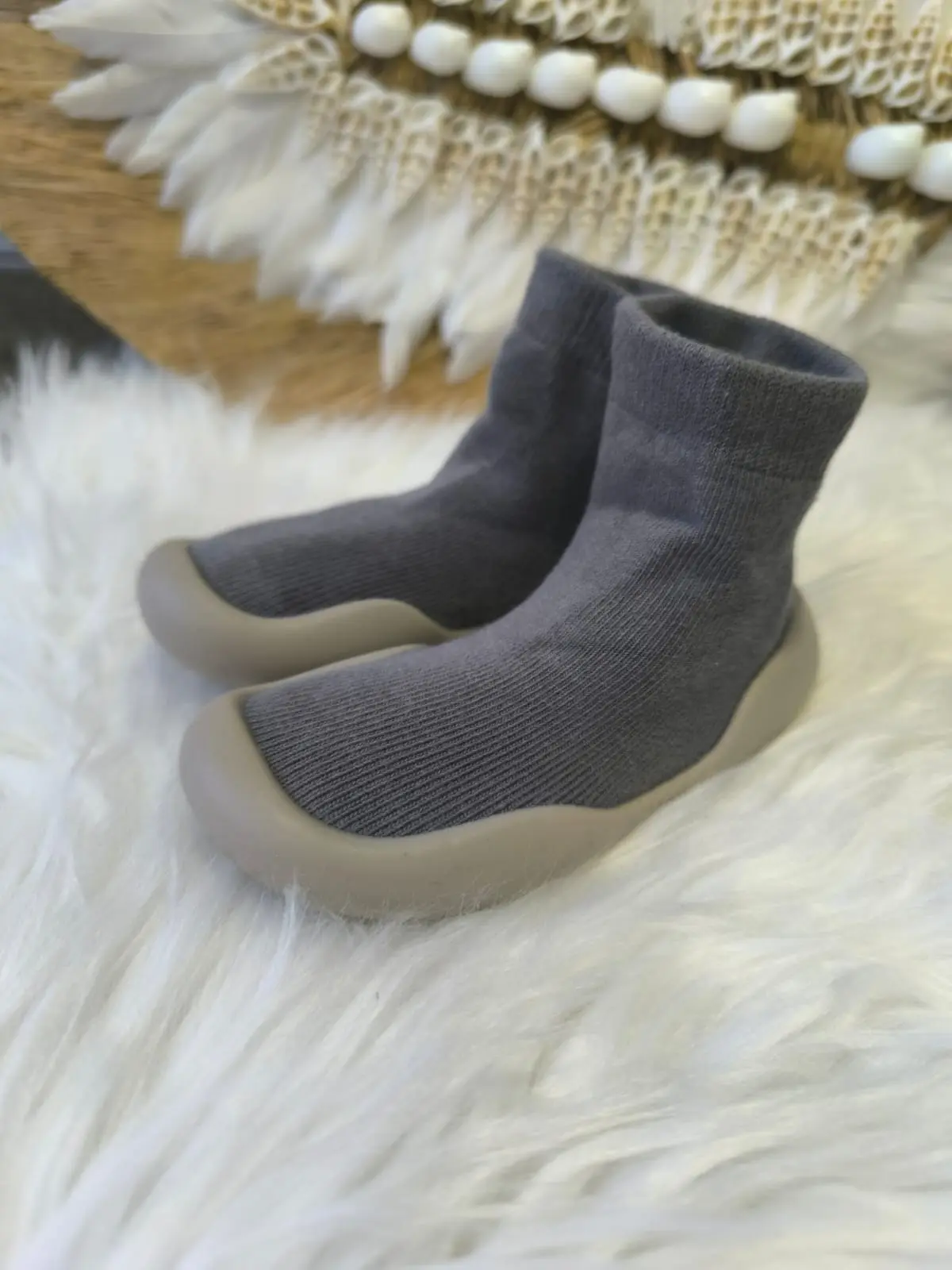 Zapatos respetuosos grises para bebé con suela de goma, textura tejida, sobre manta de pelo blanco.