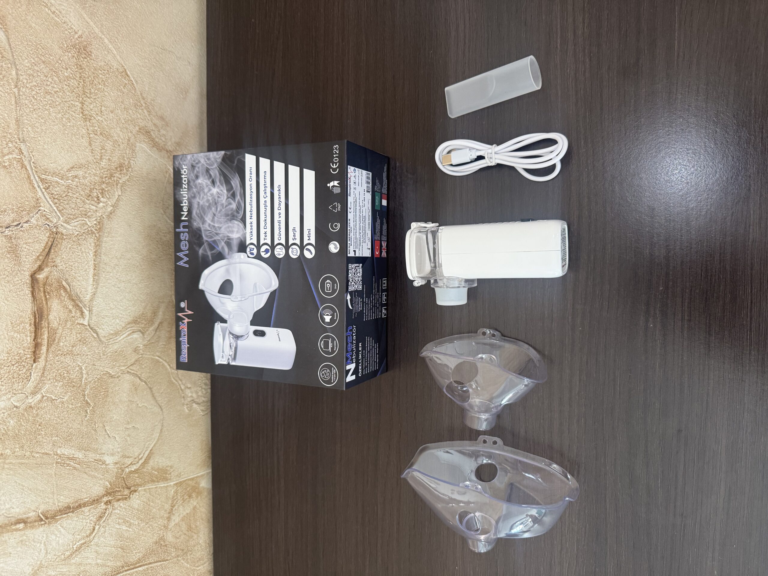 Nebulizador ultrasónico portátil blanco con accesorios transparentes y cable USB sobre superficie de madera oscura.