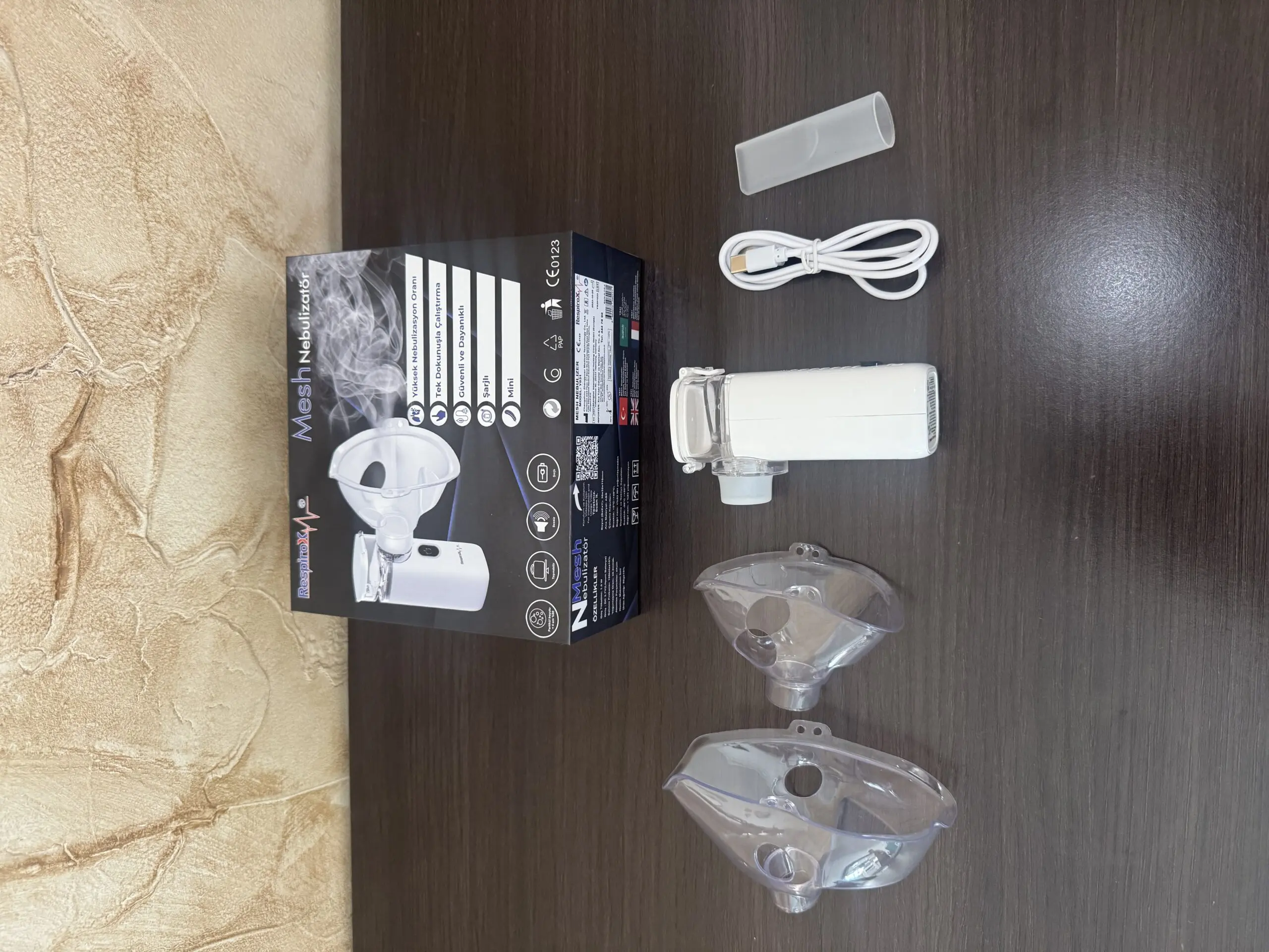 Nebulizador ultrasónico portátil blanco con accesorios transparentes y cable USB sobre superficie de madera oscura.
