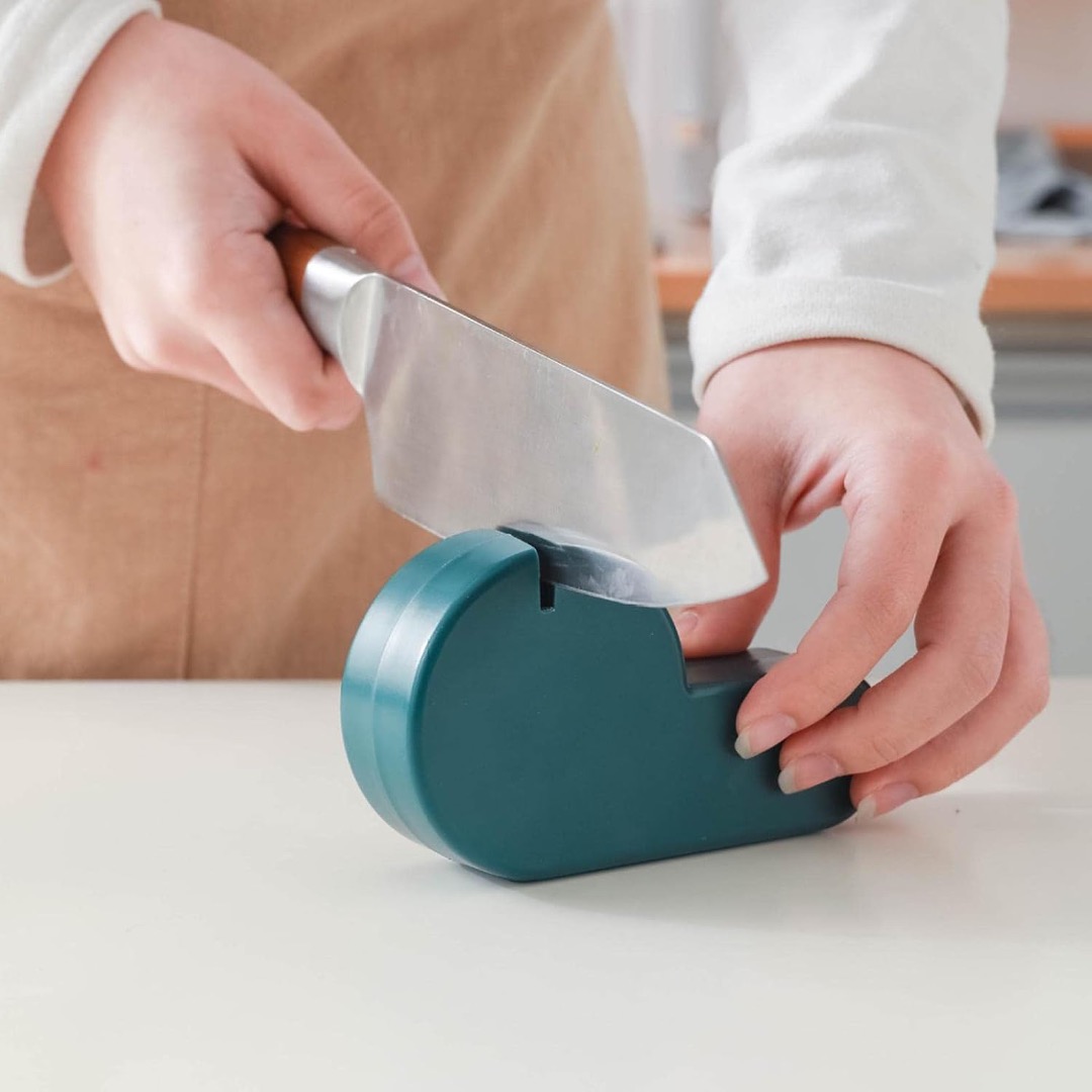 Afilador de cuchillos manual verde oscuro, con cuchillo en uso, ideal para cocina.