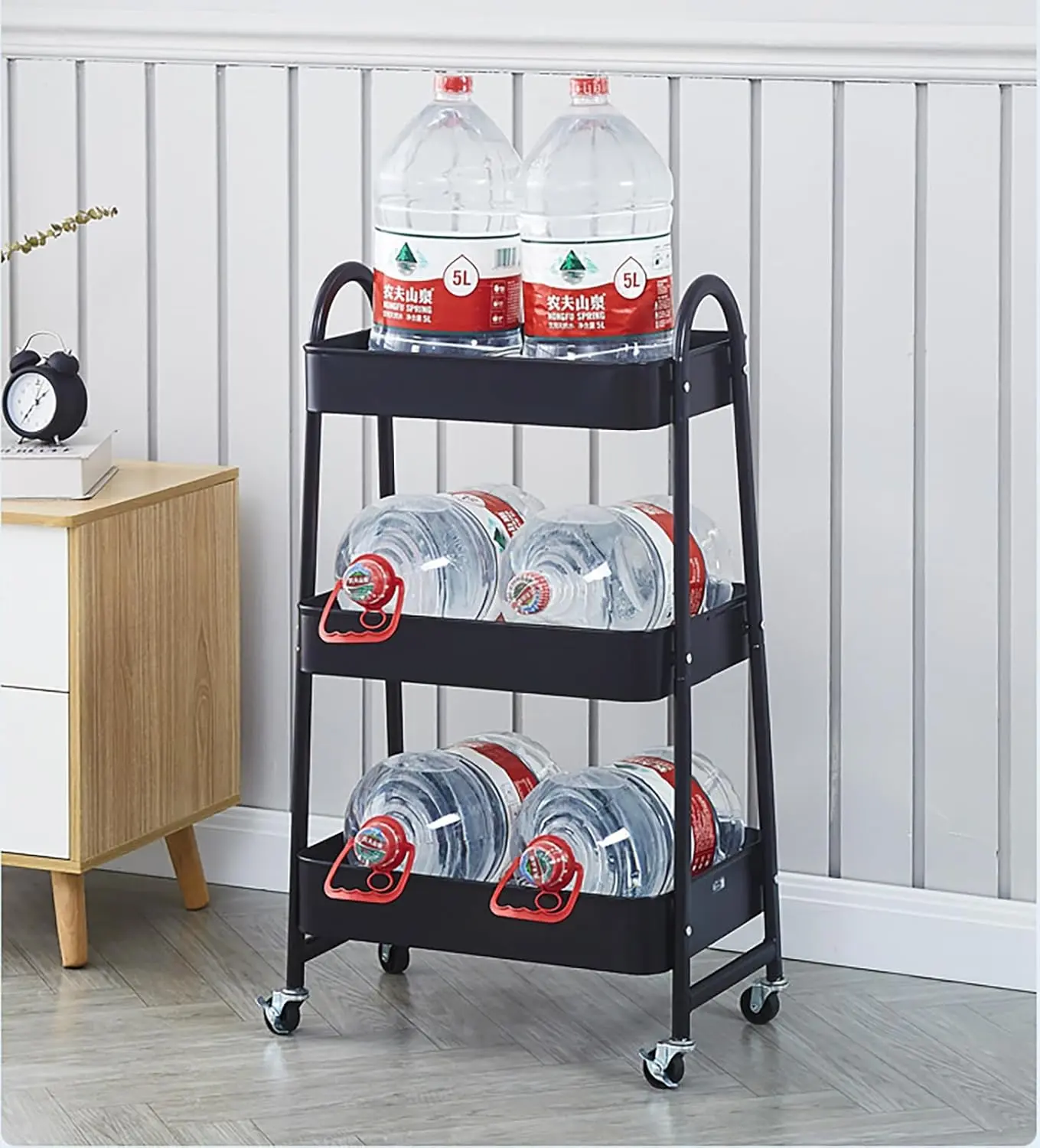 Carrito organizador negro de 3 niveles con 6 botellas de agua de 5L en un hogar.