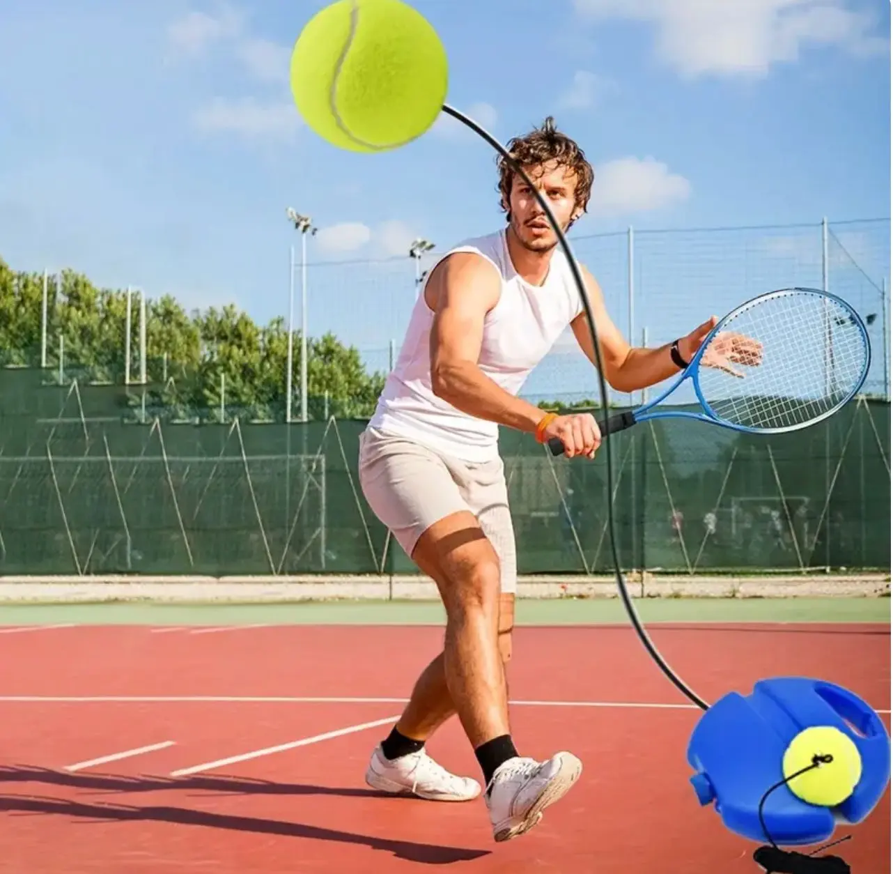 Hombre entrenando tenis con pelota atada a base azul en cancha roja.