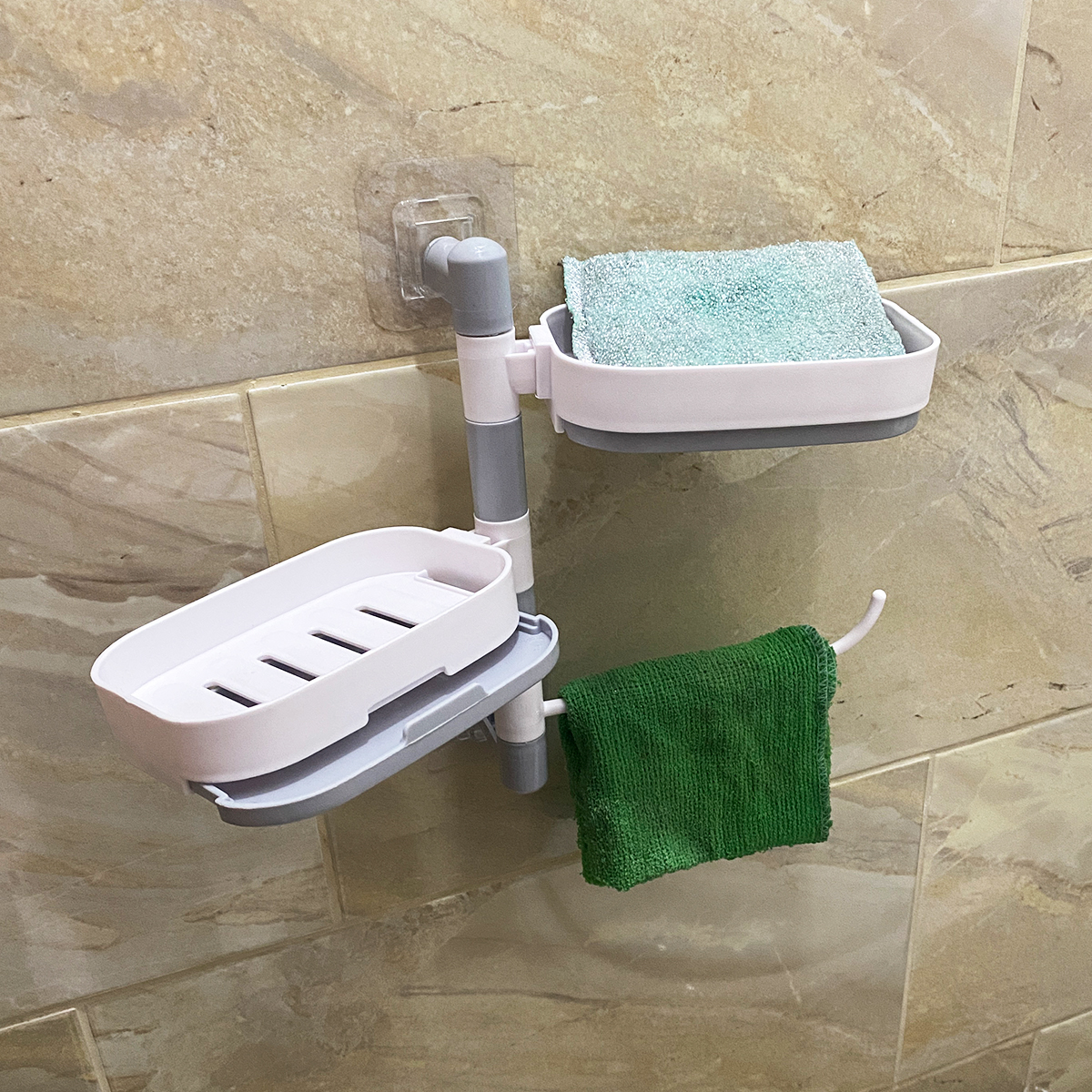 Jabonera de pared de 2 niveles, blanca y gris, con esponja azul y toalla verde.