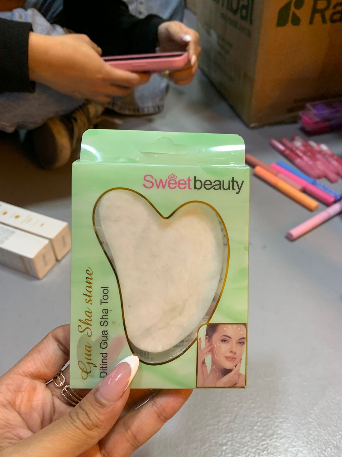 Piedra Gua Sha en forma de corazón, blanca, para masaje facial, en empaque verde de Sweet Beauty.
