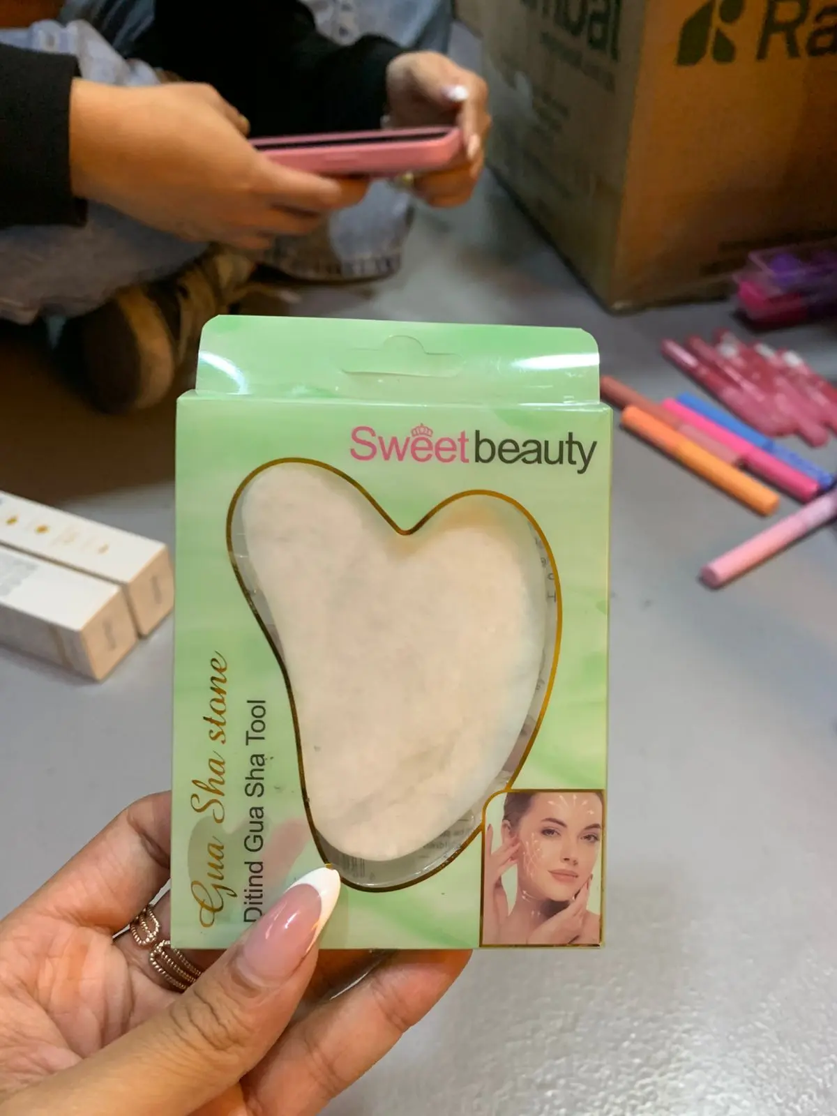 Piedra Gua Sha en forma de corazón, blanca, para masaje facial, en empaque verde de Sweet Beauty.