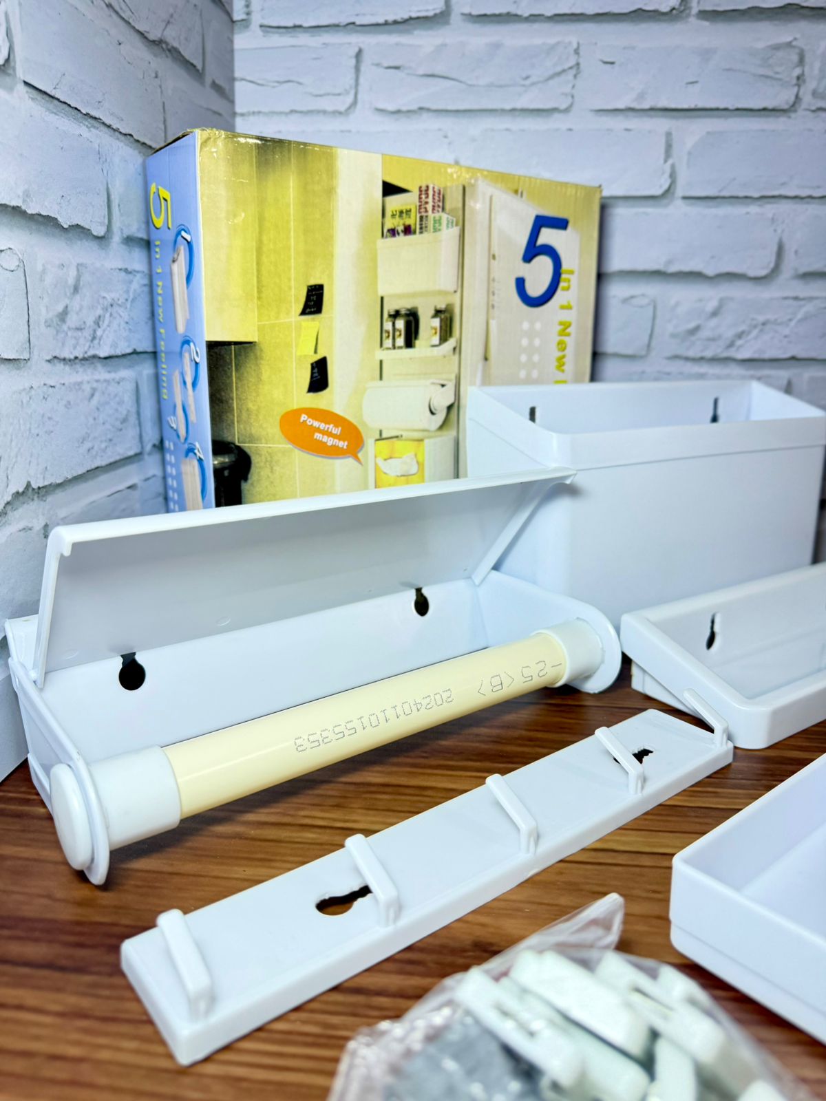 Organizador de nevera blanco magnético con soporte para rollo y caja, sobre madera, al lado de caja de producto.