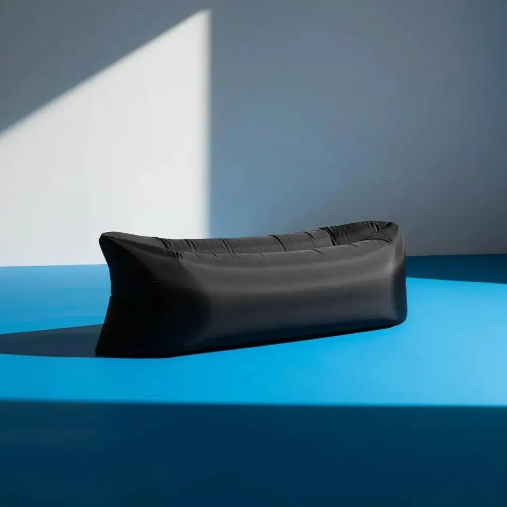 Sofá inflable portátil negro de nylon ripstop, con sombra proyectada, sobre superficie azul.