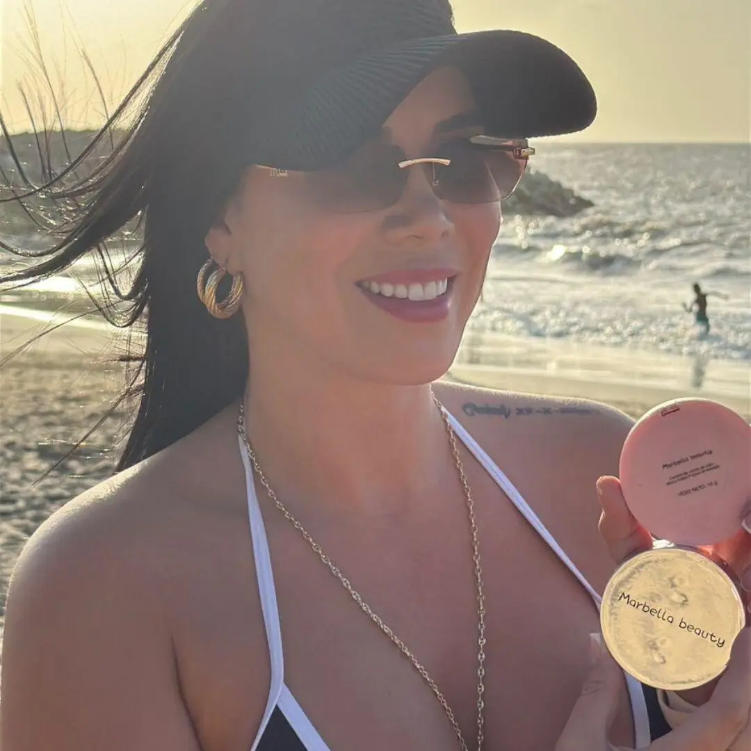 Mujer sonriente en la playa sostiene un matificante facial Marbella Beauty rosado y dorado de 10g.