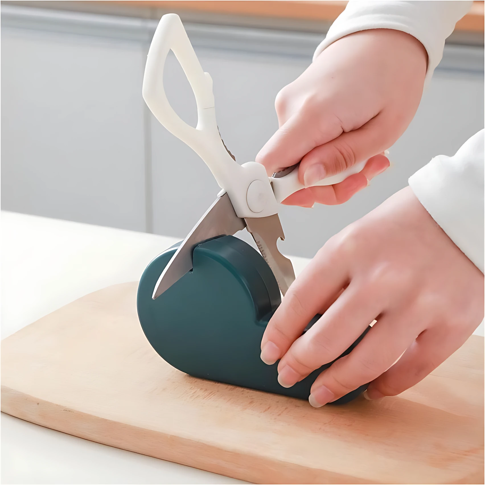 Afilador de cuchillos manual verde con tijeras blancas en uso sobre tabla de madera.