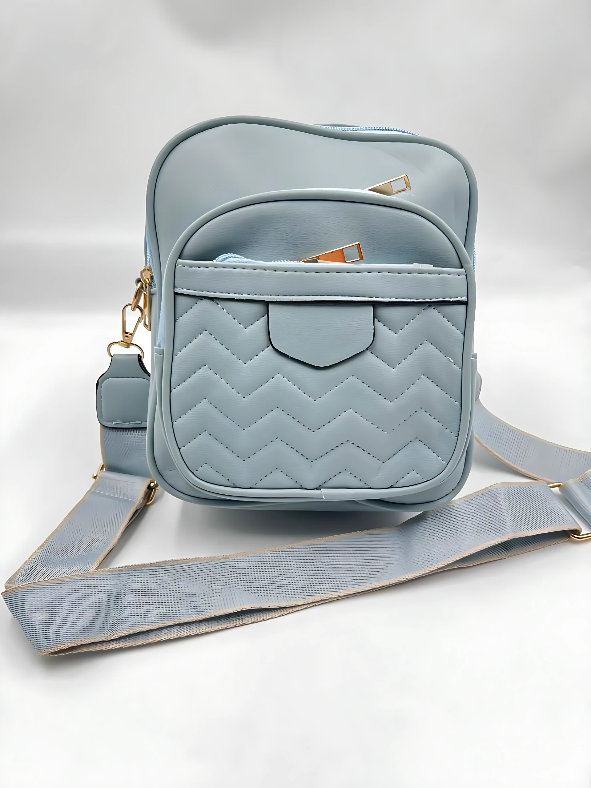 Bolso manos libres azul pastel acolchado con dos compartimentos y correa ajustable.