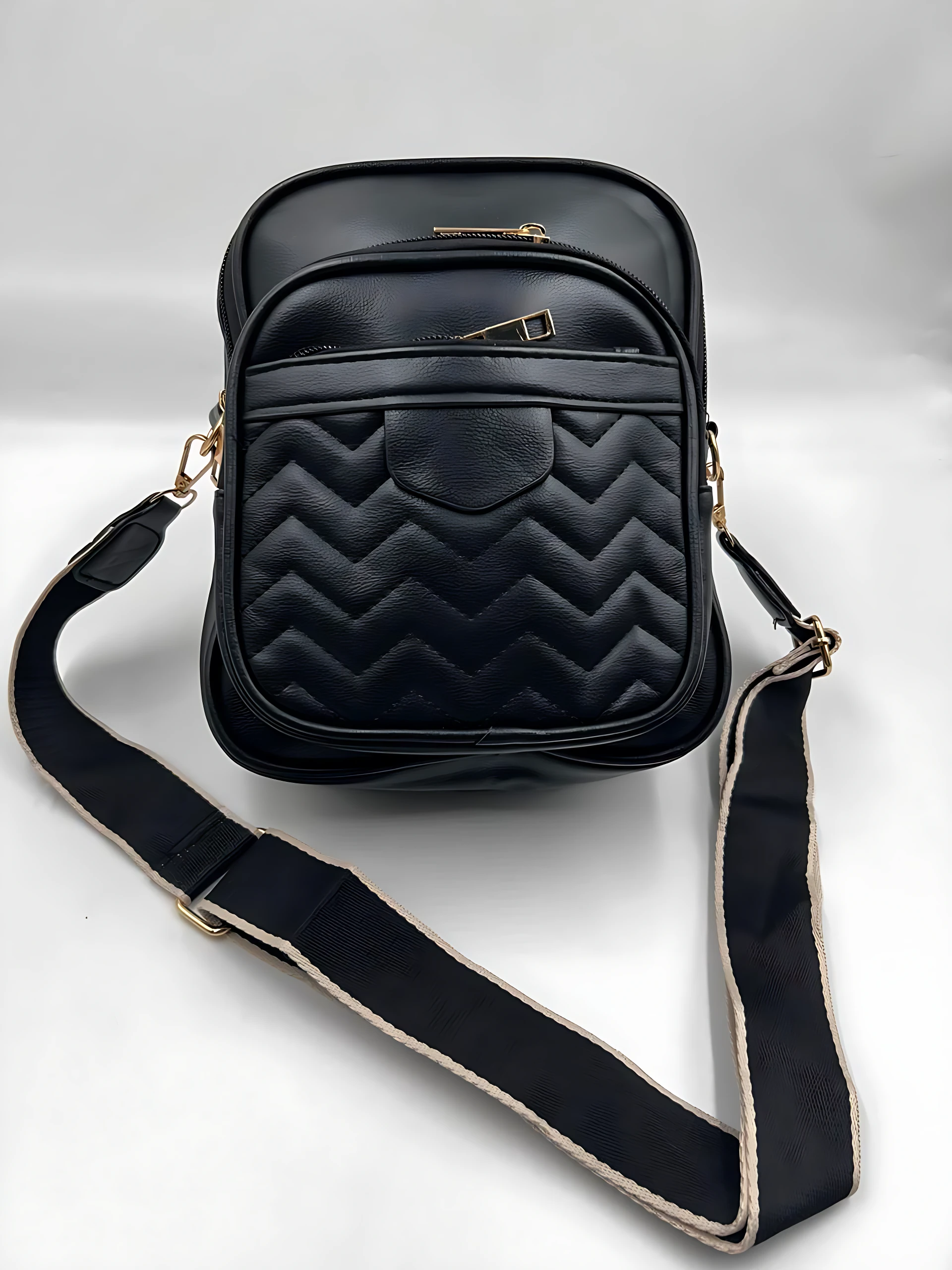 Bolso manos libres negro mujer con diseño acolchado en zigzag, dos compartimentos, correa ajustable y herrajes dorados.
